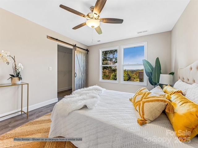 bedroom featuring visible vents, a ceiling fan, wood finished floors, a barn door, and baseboards