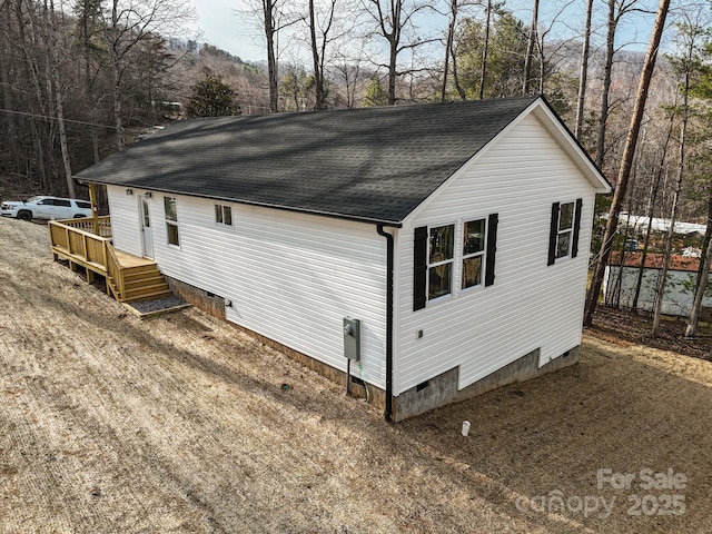 view of side of home with crawl space and roof with shingles