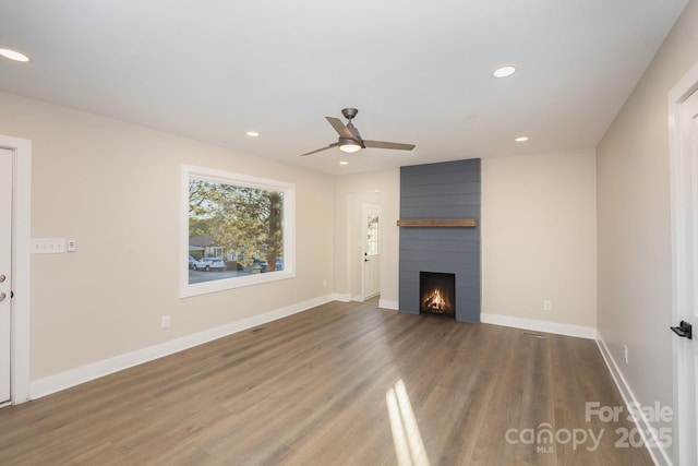 unfurnished living room with hardwood / wood-style flooring, a large fireplace, and ceiling fan