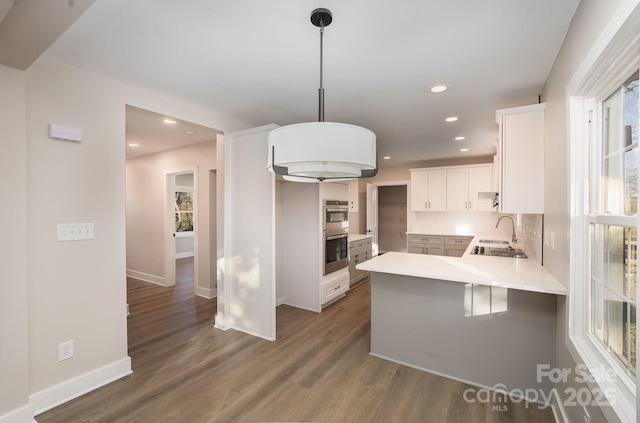 kitchen featuring decorative light fixtures, dark hardwood / wood-style floors, kitchen peninsula, decorative backsplash, and white cabinets