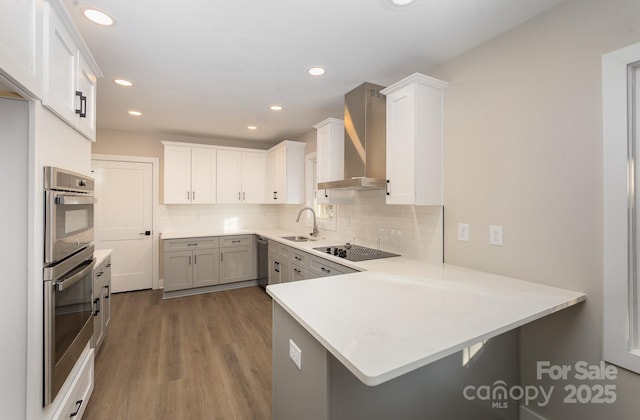 kitchen featuring appliances with stainless steel finishes, sink, a kitchen breakfast bar, kitchen peninsula, and wall chimney exhaust hood