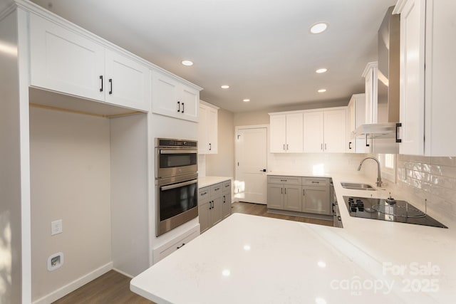 kitchen with sink, double oven, black electric stovetop, white cabinets, and decorative backsplash