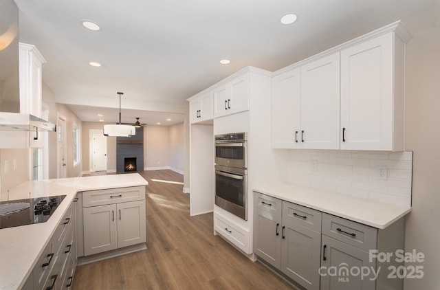 kitchen with black electric cooktop, stainless steel double oven, wall chimney exhaust hood, and gray cabinets