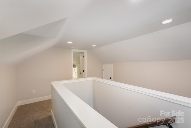 hall with lofted ceiling and dark colored carpet