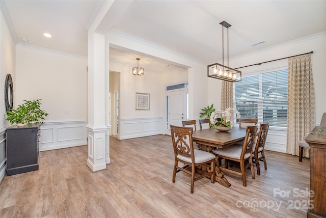 dining space featuring a notable chandelier, ornamental molding, ornate columns, and light wood-type flooring