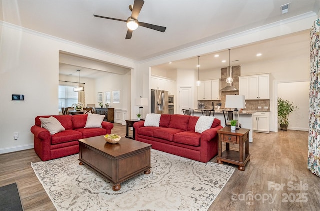 living room featuring ornamental molding, ceiling fan, and light wood-type flooring