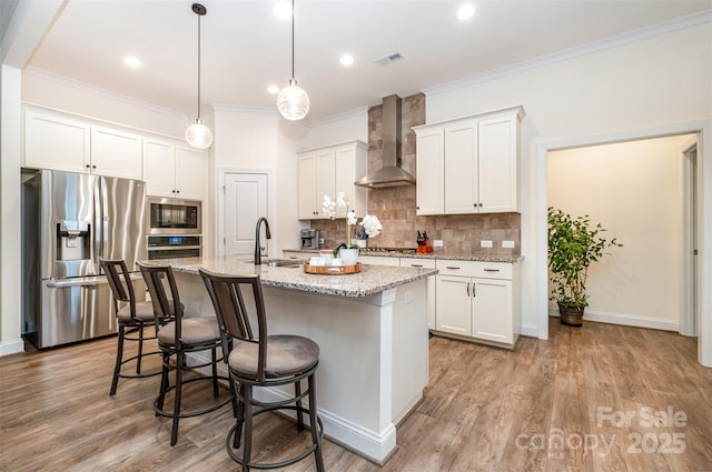 kitchen featuring sink, appliances with stainless steel finishes, a kitchen island with sink, white cabinetry, and wall chimney exhaust hood