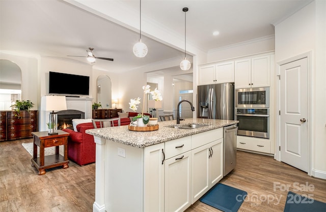 kitchen featuring appliances with stainless steel finishes, decorative light fixtures, an island with sink, sink, and white cabinets