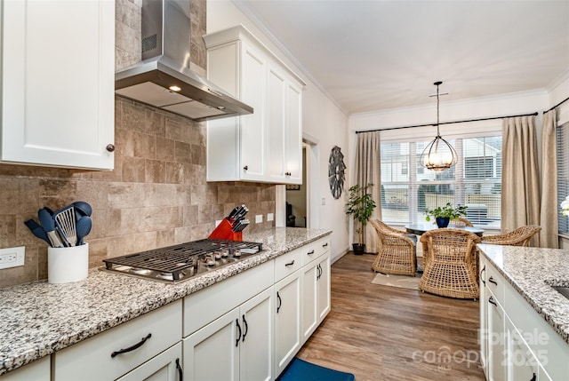 kitchen with pendant lighting, stainless steel gas stovetop, white cabinets, crown molding, and wall chimney exhaust hood