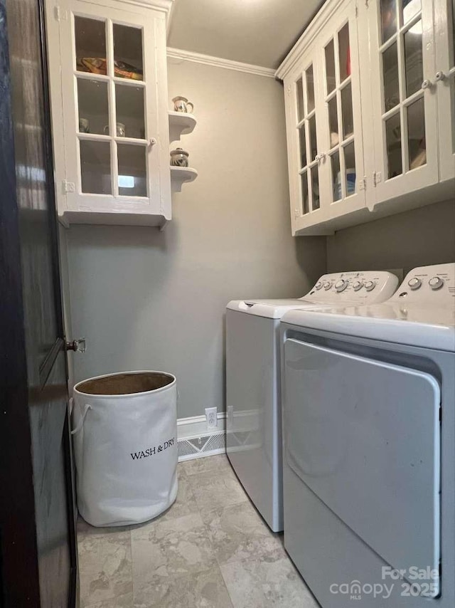 clothes washing area with cabinets, crown molding, and independent washer and dryer