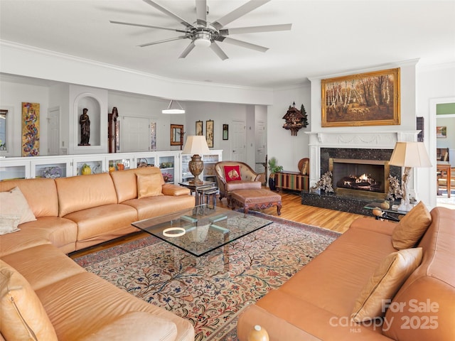 living room with a premium fireplace, ornamental molding, wood-type flooring, and ceiling fan