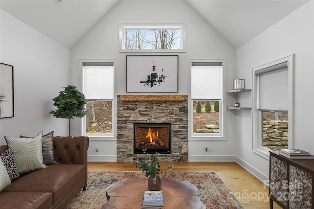 living room with light hardwood / wood-style flooring, a stone fireplace, a wealth of natural light, and lofted ceiling