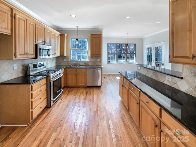 kitchen with sink, crown molding, appliances with stainless steel finishes, decorative light fixtures, and dark stone counters