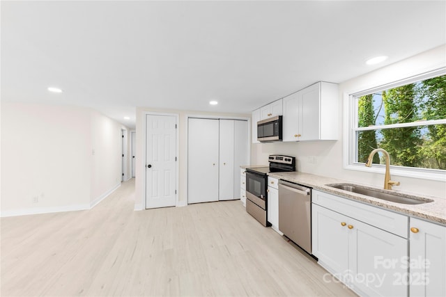 kitchen with sink, stainless steel appliances, light hardwood / wood-style floors, light stone countertops, and white cabinets