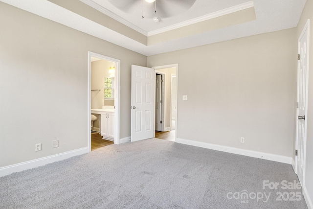 unfurnished bedroom with ensuite bath, ceiling fan, ornamental molding, light colored carpet, and a raised ceiling