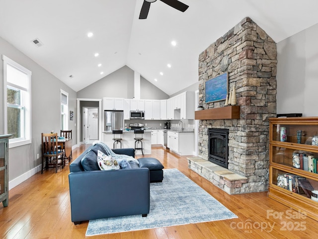 living room featuring sink, a fireplace, high vaulted ceiling, and light wood-type flooring