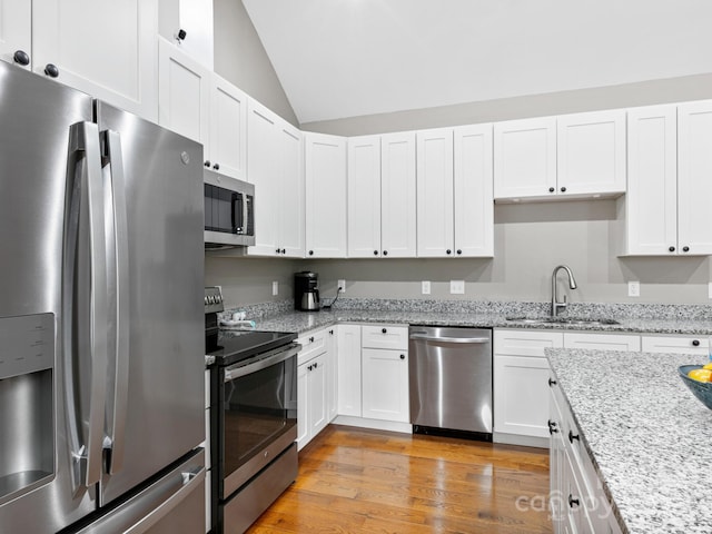 kitchen with sink, light stone counters, vaulted ceiling, appliances with stainless steel finishes, and white cabinets