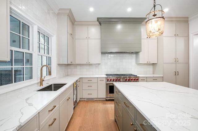 kitchen featuring sink, gray cabinets, hanging light fixtures, premium stove, and wall chimney exhaust hood