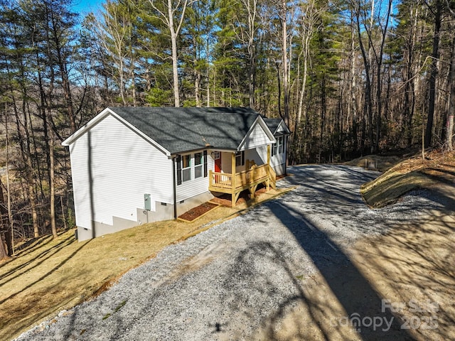 view of outbuilding featuring gravel driveway, a porch, and a wooded view