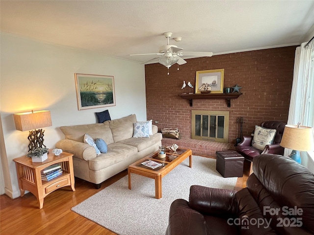 living area featuring brick wall, a fireplace, wood finished floors, and a ceiling fan