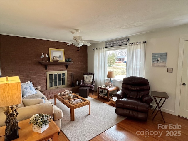 living area with ceiling fan, brick wall, wood finished floors, baseboards, and a brick fireplace