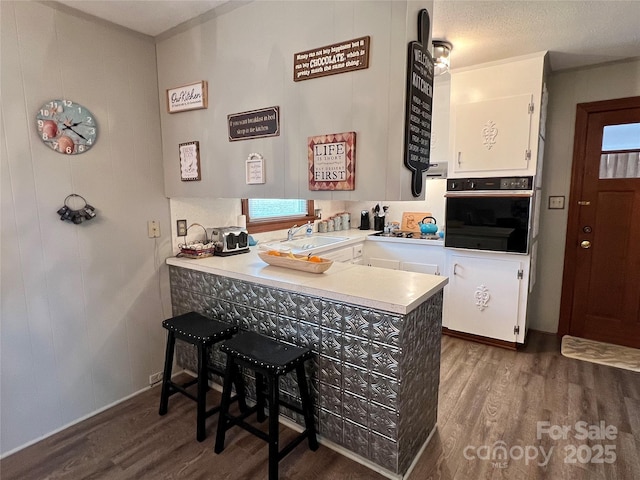 kitchen with white cabinetry, a sink, wood finished floors, black oven, and a peninsula