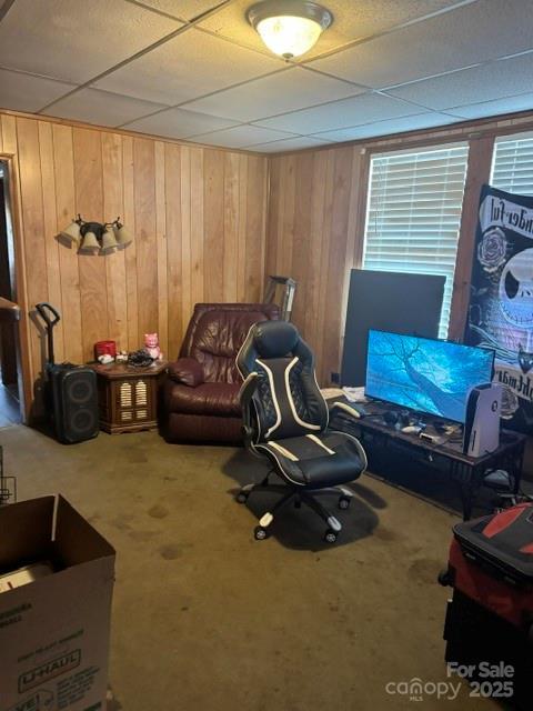 interior space featuring a paneled ceiling, wood walls, and carpet