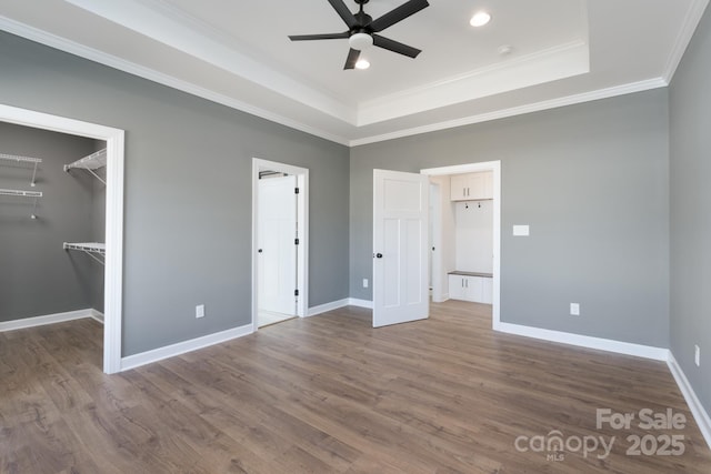 unfurnished bedroom with crown molding, a spacious closet, wood-type flooring, and a tray ceiling