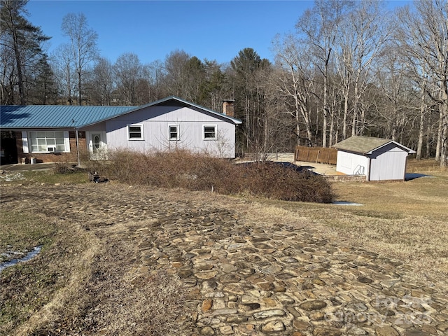 view of property exterior with a shed, a chimney, metal roof, and an outbuilding