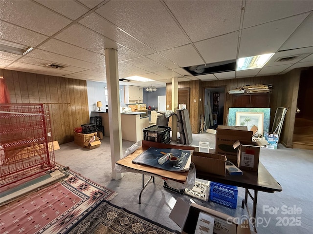 finished basement with a paneled ceiling, wood walls, and visible vents