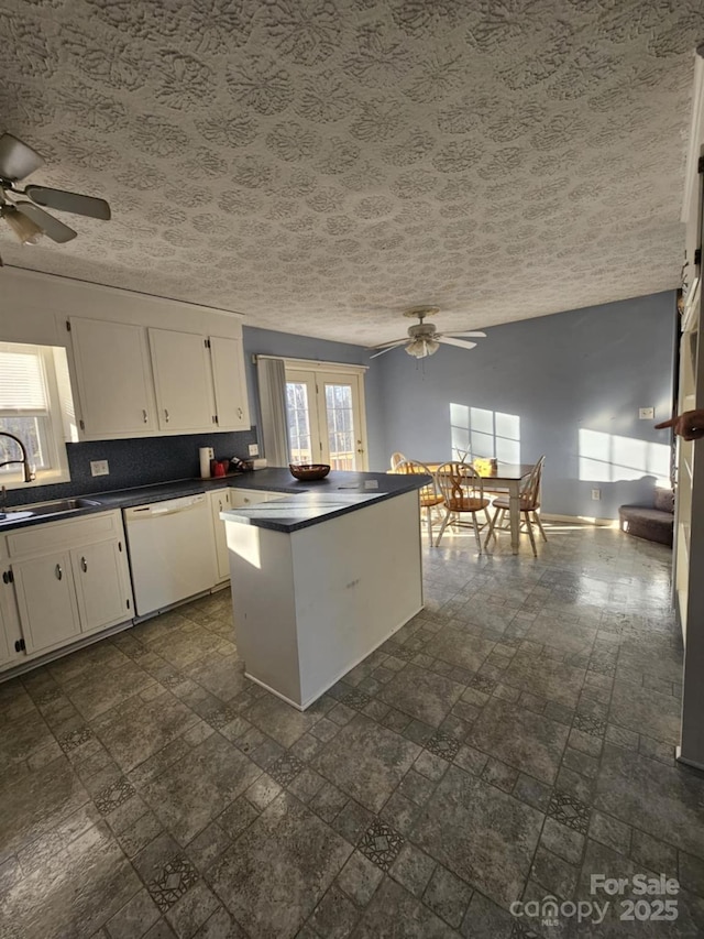 kitchen with white cabinets, dark countertops, a peninsula, white dishwasher, and a sink