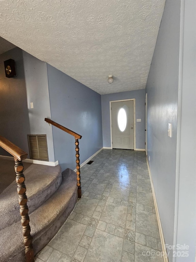 foyer entrance with visible vents, a textured ceiling, baseboards, and stairs