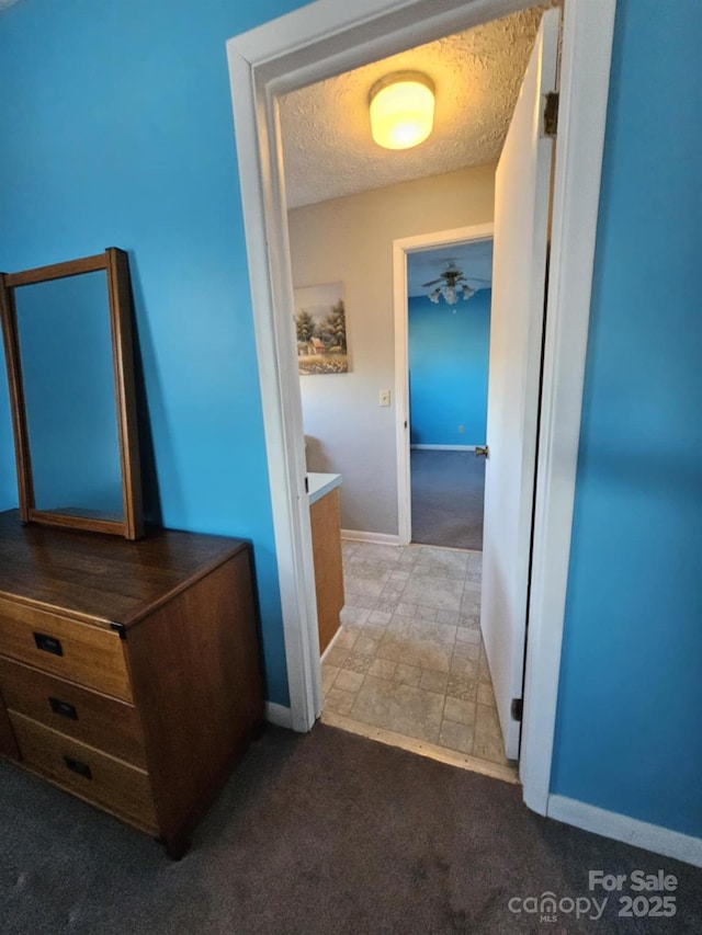 corridor featuring a textured ceiling, baseboards, and carpet flooring