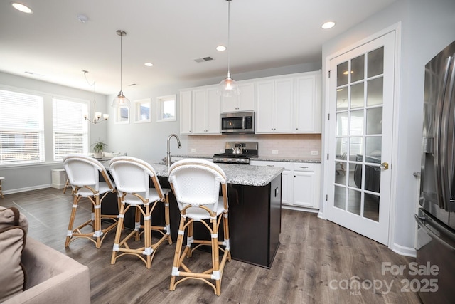 kitchen featuring white cabinetry, a center island with sink, hanging light fixtures, light stone countertops, and appliances with stainless steel finishes