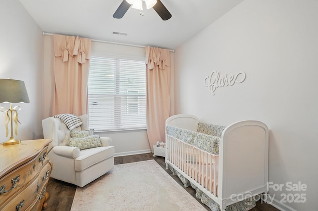 bedroom with visible vents, baseboards, a ceiling fan, wood finished floors, and a crib