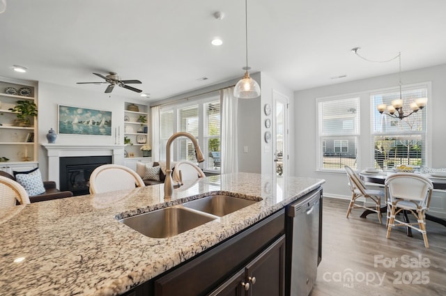 kitchen featuring stainless steel dishwasher, hanging light fixtures, a sink, and light wood-style floors
