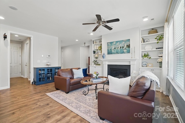 living room with a ceiling fan, a glass covered fireplace, wood finished floors, and a healthy amount of sunlight