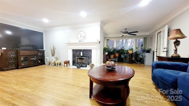 living room with ornamental molding, a wood stove, ceiling fan, and light wood-type flooring