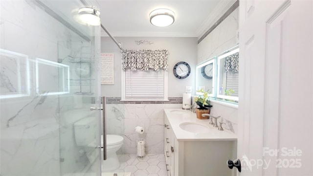 bathroom featuring toilet, crown molding, tile walls, vanity, and a shower with door