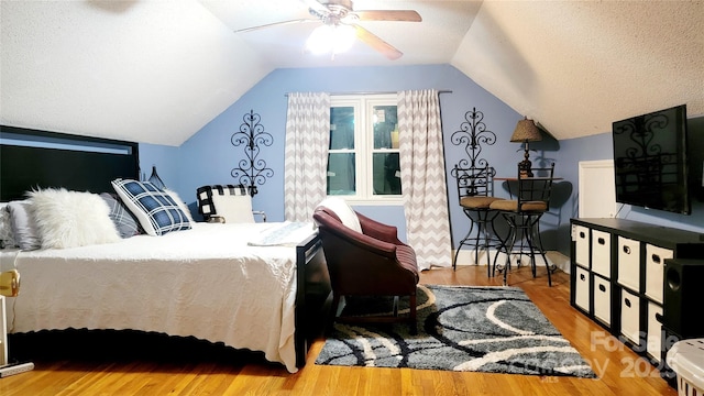 bedroom featuring vaulted ceiling, light hardwood / wood-style floors, and a textured ceiling