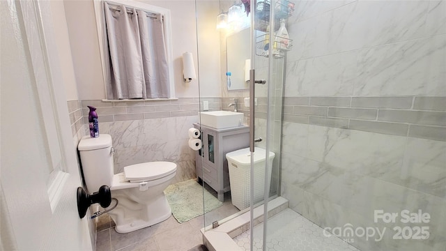 bathroom with sink, a shower with door, tile walls, tile patterned floors, and toilet