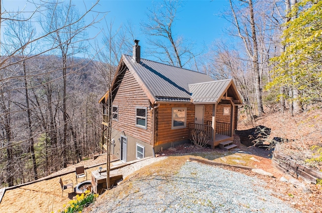 view of home's exterior featuring log siding, metal roof, driveway, and a chimney