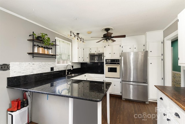 kitchen featuring sink, white cabinetry, stainless steel appliances, kitchen peninsula, and dark stone counters