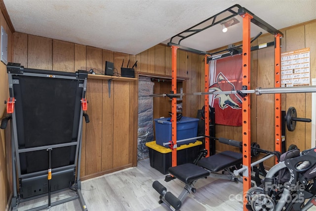 exercise area with light hardwood / wood-style floors, a textured ceiling, and wood walls