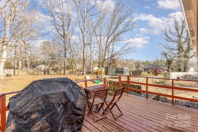 wooden deck featuring a playground, a grill, and a trampoline