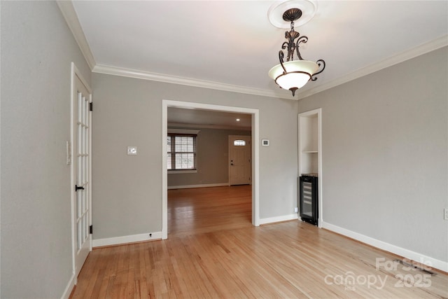 spare room with crown molding, beverage cooler, and light hardwood / wood-style flooring