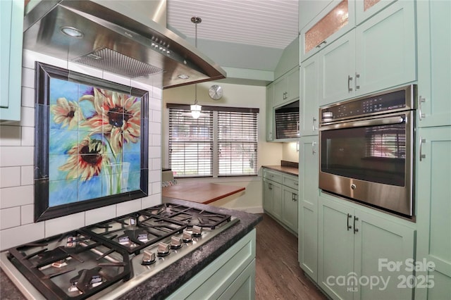 kitchen with stainless steel appliances, pendant lighting, green cabinetry, and wall chimney exhaust hood