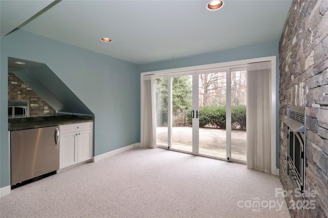 unfurnished living room with a stone fireplace, light colored carpet, and french doors