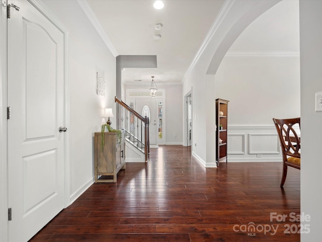 foyer entrance with ornamental molding, arched walkways, wood-type flooring, baseboards, and stairs