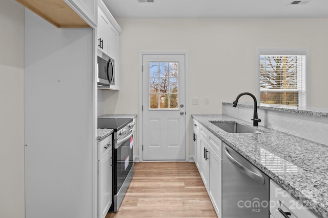 kitchen with sink, white cabinets, light stone counters, stainless steel appliances, and light wood-type flooring